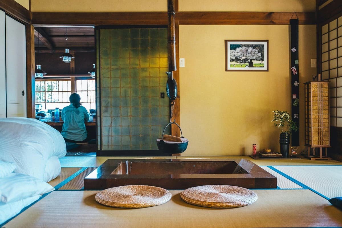 Ruangan tradisional Jepang dengan tatami, irori, dan seseorang duduk di balik pintu geser.
